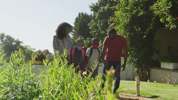 African american family wearing face mask walking in the garden holding hands together on a bright s