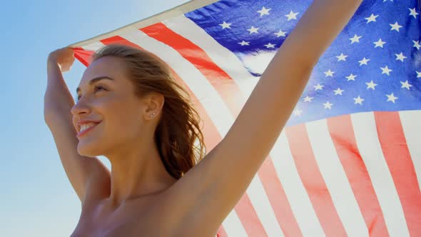 Side view of young Caucasian woman holding a American flag on the beach 4k