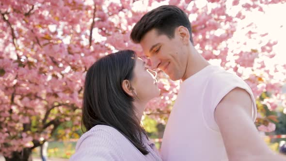 Romantic couple taking selfie video by sunset over the blooming sakura park in Japan. 