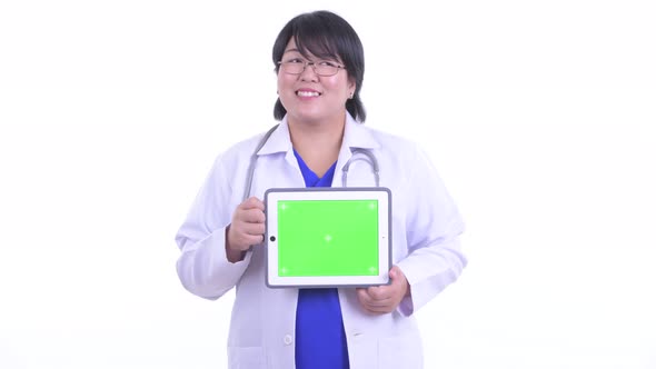 Happy Overweight Asian Woman Doctor Thinking While Showing Digital Tablet