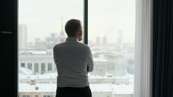 businessman stands with his back and looks out the window at city view