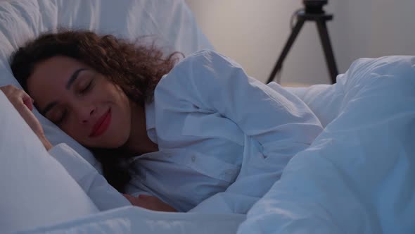 Latino beautiful woman lying down on bed in bedroom in dark night room.