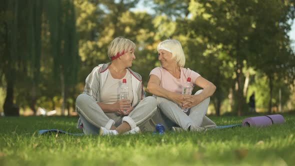 Two Women Sitting on Grass and Smiling Into Camera After Finishing Doing Yoga