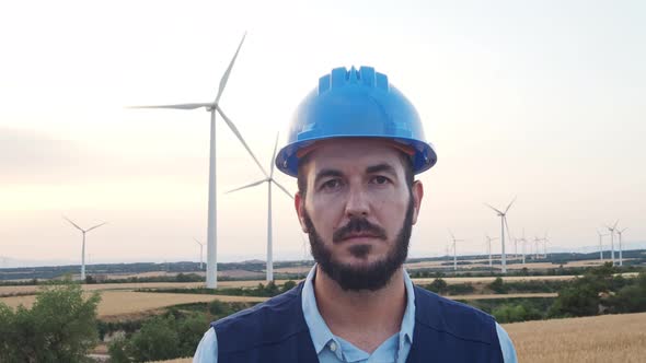 Young Engineer Man Ooking Seriously at Camera in a Field of Windmills