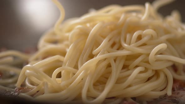 Camera follows adding spaghetti on cooked bacon in a pan. Slow Motion.