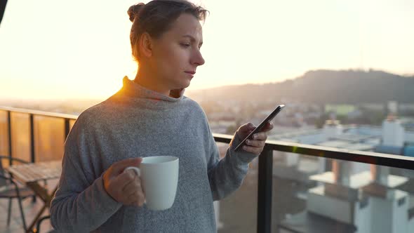 Woman Starts Her Day with a Cup of Tea or Coffee and Checking Emails in Her Smartphone on the