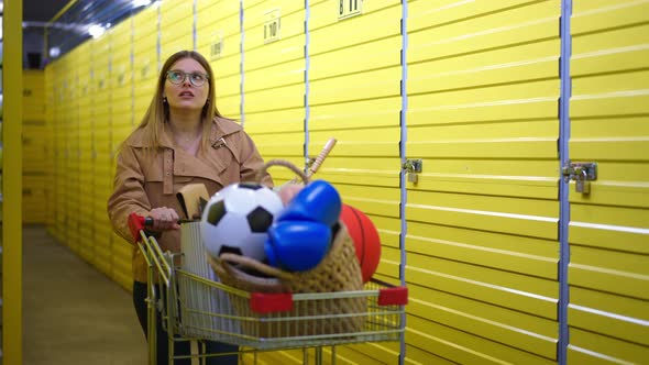 Unsure Young Caucasian Woman Passing with Trolley in Self Storage Leaving