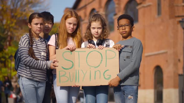 Schoolkids Standing Outdoors with Stop Bullying Cardboard Banner