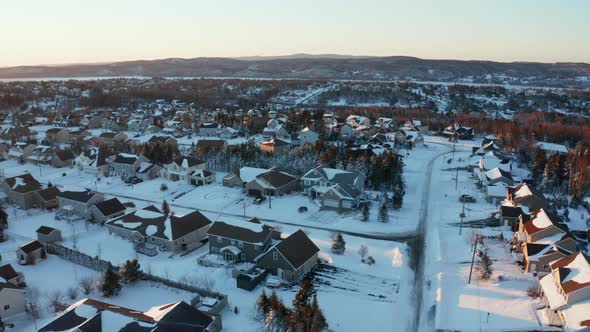 Picturesque winter aerial flying over a snowy suburban neighborhood at dusk.