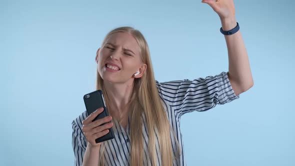 Young Blonde Woman Getting High While Listening To the Music and Singing on Blue Background