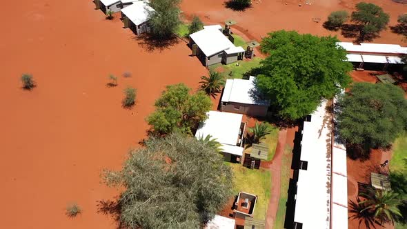 Backwards drone shot of a lodge in Namibia with small houses and a pool. In the middle of the lodge