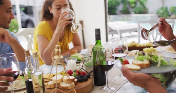 Group of diverse male and female friends drinking wine and talking at dinner party on patio