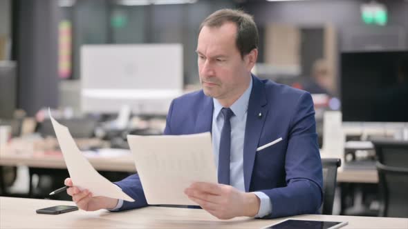 Businessman Reading Reports While Sitting in Office