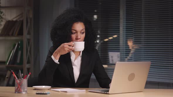 Portrait of African American Woman Typing on Laptop and Drinking Coffee