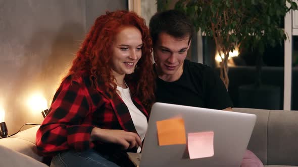 Beautiful Young Couple Sitting Together with Grey Laptop on Couch