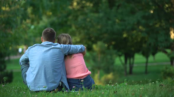 Back View of Young Couple Hugging and Sitting on Grass at Park, Togetherness