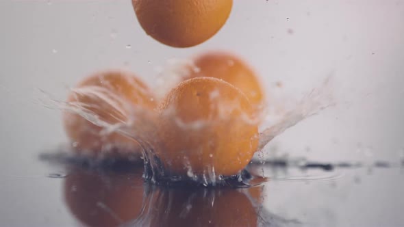 Fresh oranges fall onto a surface covered with clean water