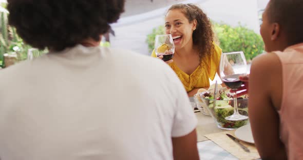 Group of diverse male and female friends dining, laughing and drinking wine at dinner party on patio