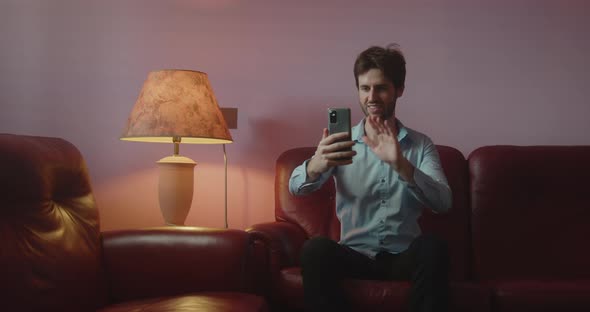 Boy greets with smartphone while video call on sofa at home