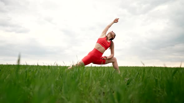 Sporty Woman in Orange Costume Practicing Yoga in Green Fresh Field Minimalist Scene