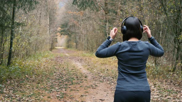 Sporty woman puts on headphones and activates fitness app on her smartwatch for running through the