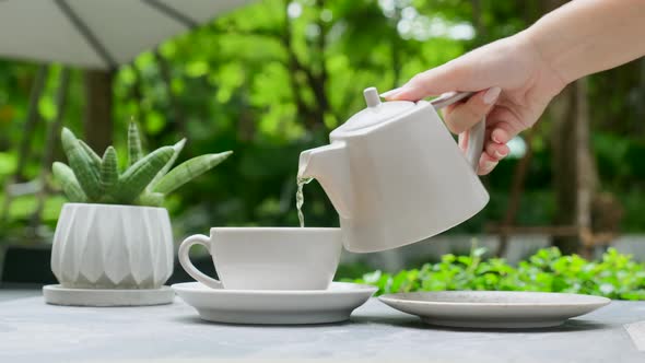 Waiter Pouring Hot Tea of Teapot Into Cup in Outdoors Restaurant Woman Hand