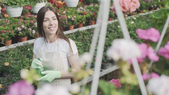 Girl sprays flowers in the garden. Caucasian woman takes care of plants by moisturizing them. Slow m