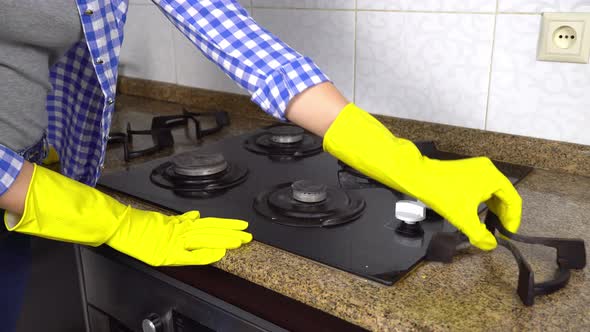 housewife woman in yellow gloves washes gas stove in kitchen with sponge.