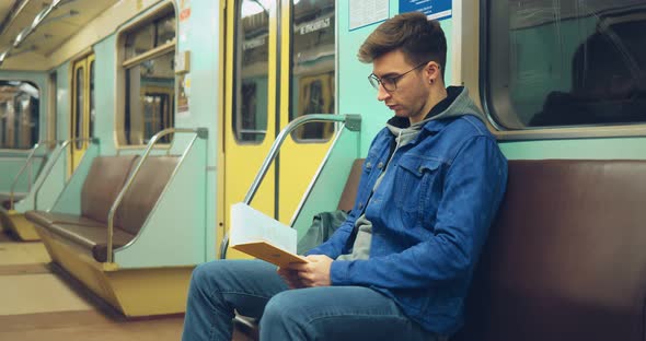 Young Handsome Man Reading a Book in the Subway Car