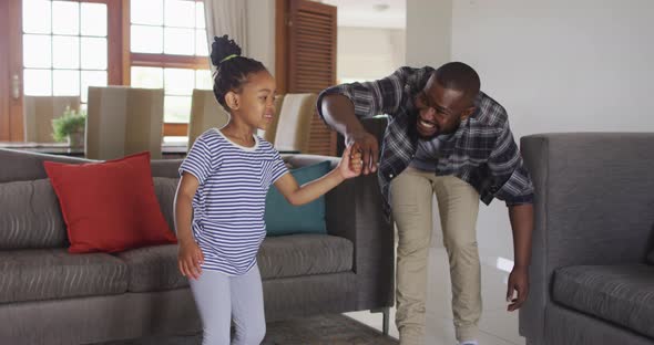 Happy african american daughter and father having fun, dancing in living room