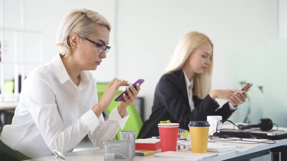 Two Attractive Girls Use Smartphones To Perform Work Tasks