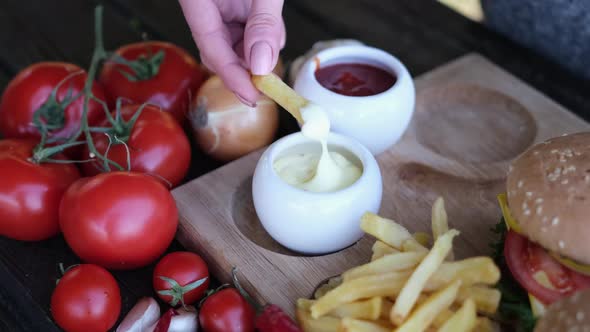 Dipping French Fries Into Garlic Dip Sauce on Wooden Board