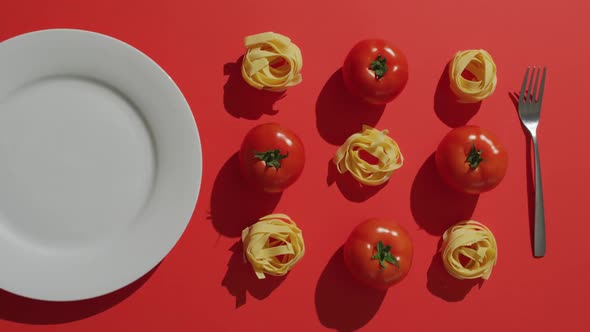 Video of fresh red tomatoes and pasta nests with plate and fork on red background