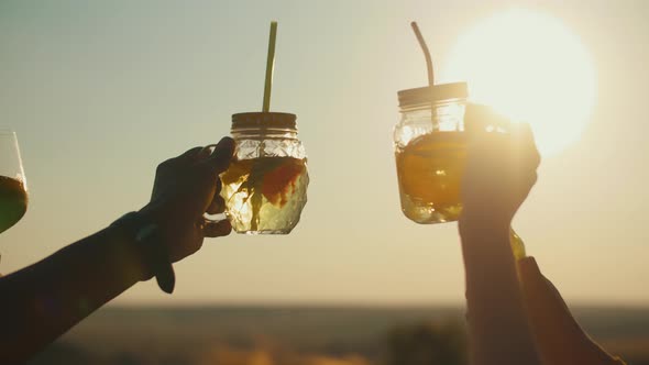 Dancing Hands Holding Glasses with Cocktail Closeup Against Background of the Sky and Bright