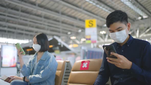 Social distancing, two people wearing face mask sit keeping distance away from each other in airport