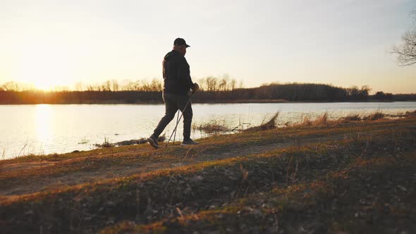 Side View a Man Sport Fitness Nordic Walking with Special Stick on the Ground Next to Water