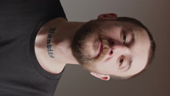 Vertical Studio Shot of a Middleaged Bearded Man with Tattoo on His Neck and Chick Nodding and