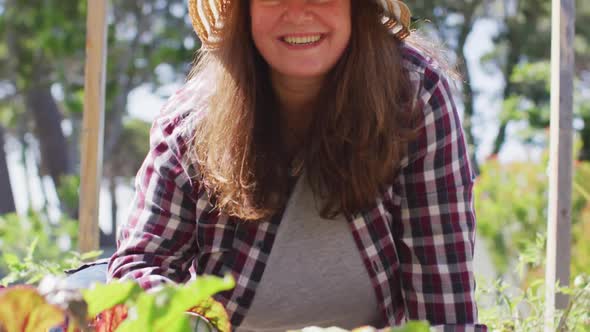 Portrait of happy caucasian woman wearing hat, gardening and smiling in garden