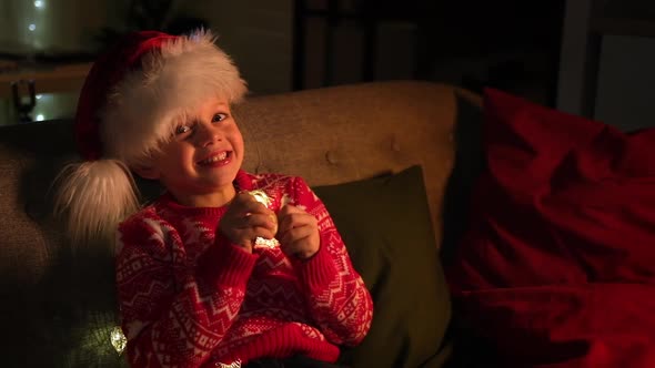 Portrait Excited Boy in Santa Hat and Christmas Costume Sitting at Home Eating Orange Tangerine