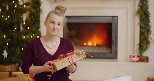 Young Woman Holding Christmas Present Against Fireplace
