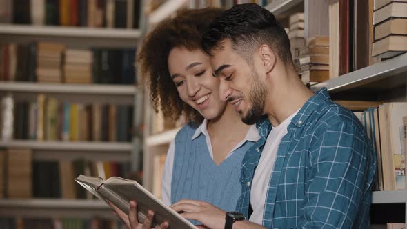 Young Couple Students Standing in University Library Laughing Reading Funny Story Hispanic Guy with