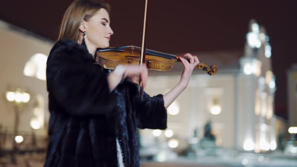 Romantic Girl in Warm Clothes is Playing a Violin in the Street 