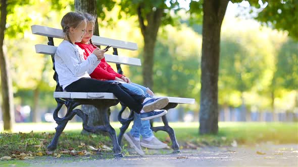 Little Adorable Girls with Smartphone in Fall. Kids Having Fun at Warm Sunny Autumn Day Outdoors