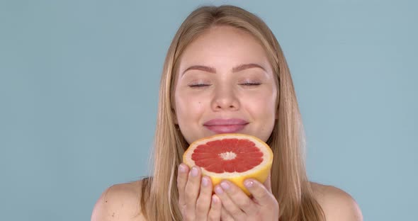 Beautiful Happy Smiling Young Blonde Woman. She Enjoys the Smell of Fresh Grapefruit