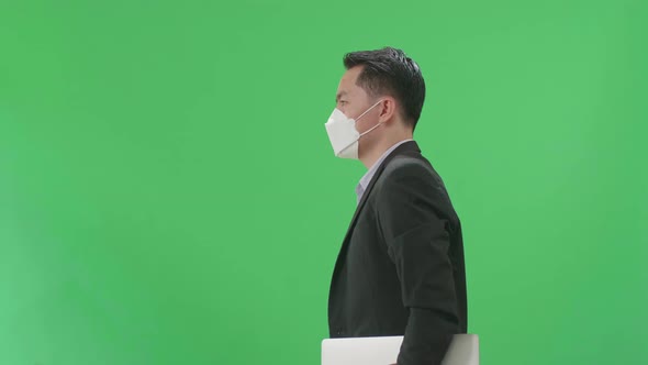 Asian Business Man Holding Book And Document While Walking On Green Screen, Wear Medical Mask