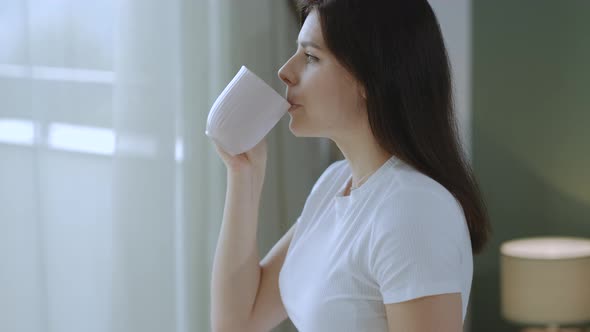 Close up of Calm brunette woman drinking tea enjoying morning time  at home