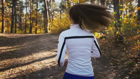 Unrecognizable Young Female in Sportswear is Running By Trail in an Autumn Wood on Sunny Day