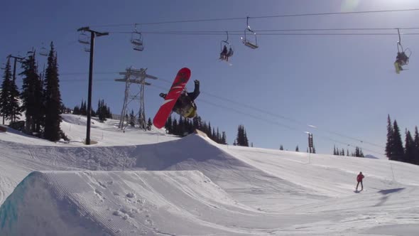 A young man snowboarder going off jumps in a terrain park.