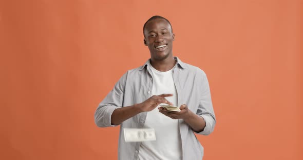 Rich Black Man Throwing Money and Laughing on Orange Background
