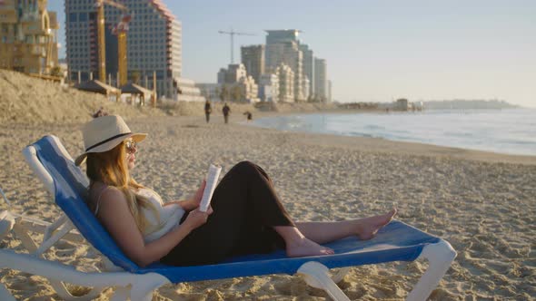 young attractive woman sitting on a beautiful beach reading a book